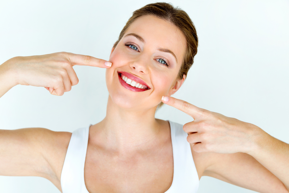 Image of a prosthodontist showing a patient a thin porcelain veneer, illustrating the "definition veneer" concept. No text on the image.